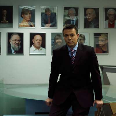 Presenter Kevin Owen in front of portraits of famous guests at the Russia Today studios
