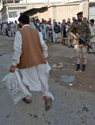 A soldier stands guard as people queue outside a flourmill in Karachi