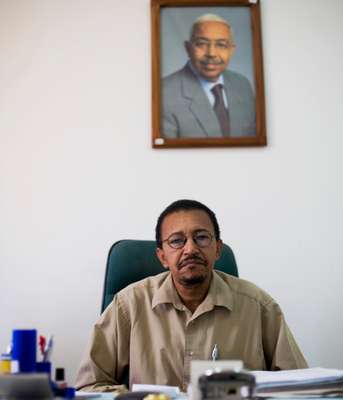 Alfredo Santos, director of InforPress agency, in front of a photograph of President Pedro Pires