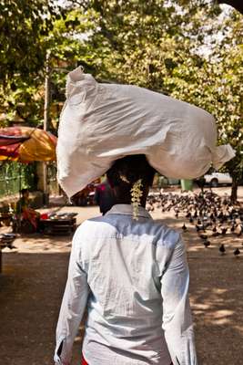 A woman carries a heavy load, with jasmine in her hair