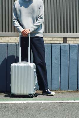 SWEATSHIRT by Studio Nicholson, TROUSERS by Make Sense Laboratory, TRAINERS by Moonstar, SUITCASE by Rimowa