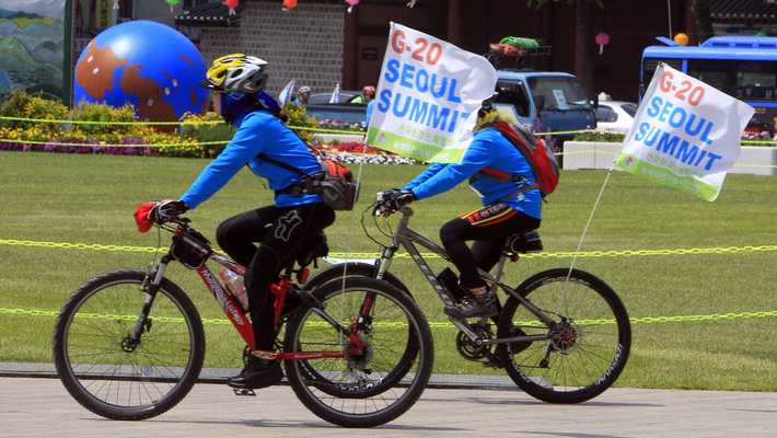Volunteers on bicycles carry G20 banners 