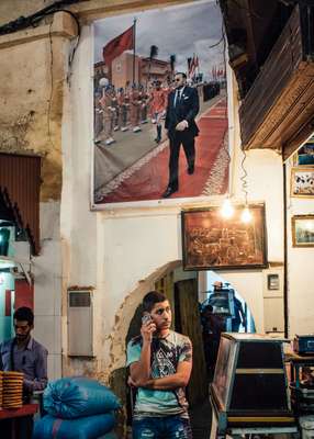 Making a phone call in the souk in Fes beneath an official poster of Mohammed VI