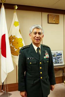 Standing before the national flag and the insignia of the GSDF – a golden cherry blossom framed by ivy