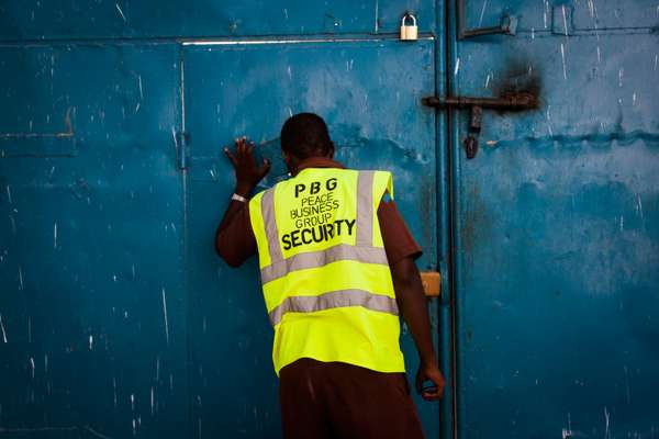 Security guard looking through a hole in a gate before allowing a car to enter the Peace Hotel 