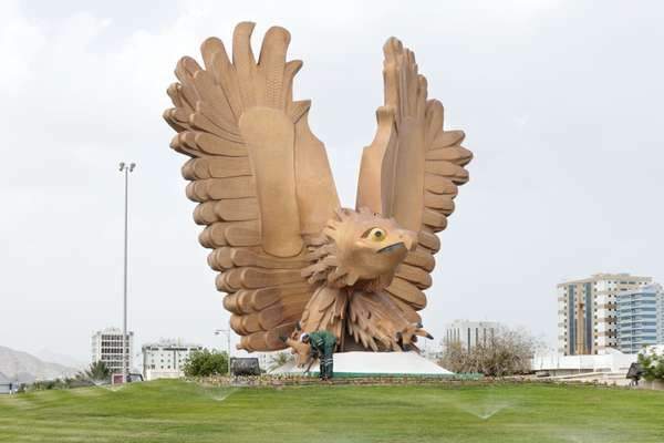 A man turns on the sprinklers at a falcon statue at a roundabout in Fujairah